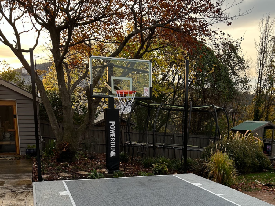 Residential basketball court featuring a PowerDunk hoop, surrounded by trees and a backyard setting, showcasing custom court surface and family-friendly space for sports activities.