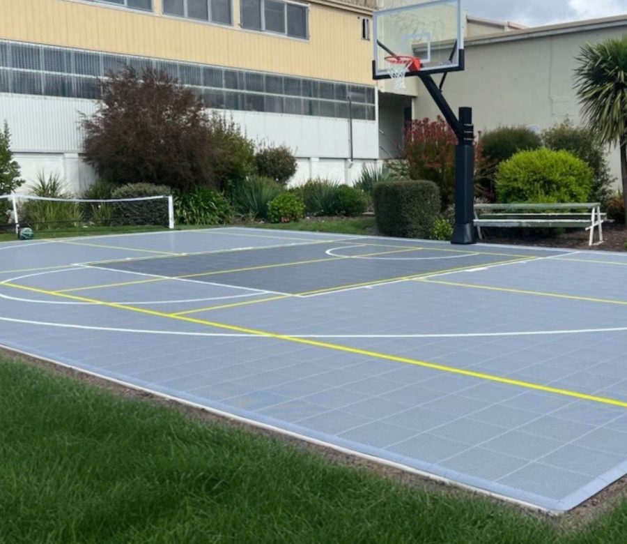 Pickleball court with multi-sport layout, featuring durable court tiles, clear line markings, and a basketball hoop, set in a landscaped backyard environment.